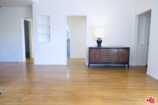 unfurnished room with built in shelves and light wood-type flooring