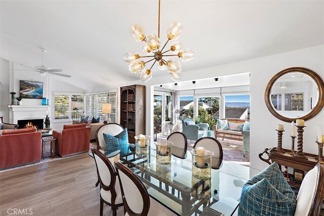 dining space featuring lofted ceiling, ceiling fan with notable chandelier, a wealth of natural light, and light hardwood / wood-style flooring