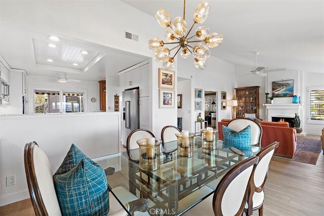 dining space featuring a raised ceiling, ceiling fan with notable chandelier, a wealth of natural light, and light hardwood / wood-style floors