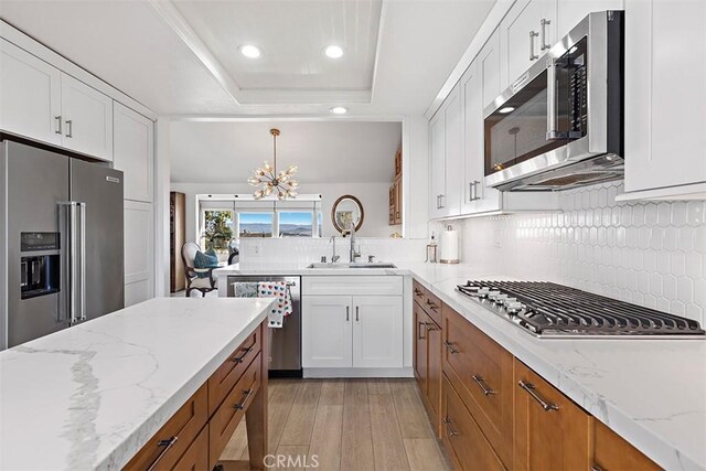 kitchen with white cabinetry, stainless steel appliances, sink, and hanging light fixtures