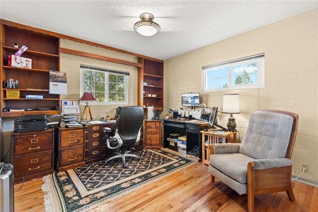 home office featuring light hardwood / wood-style floors, a textured ceiling, and brick wall