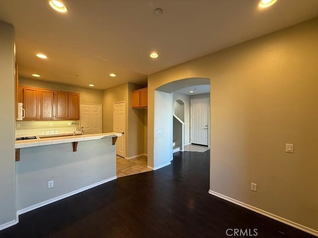 kitchen with wood-type flooring, tile countertops, a kitchen breakfast bar, and kitchen peninsula