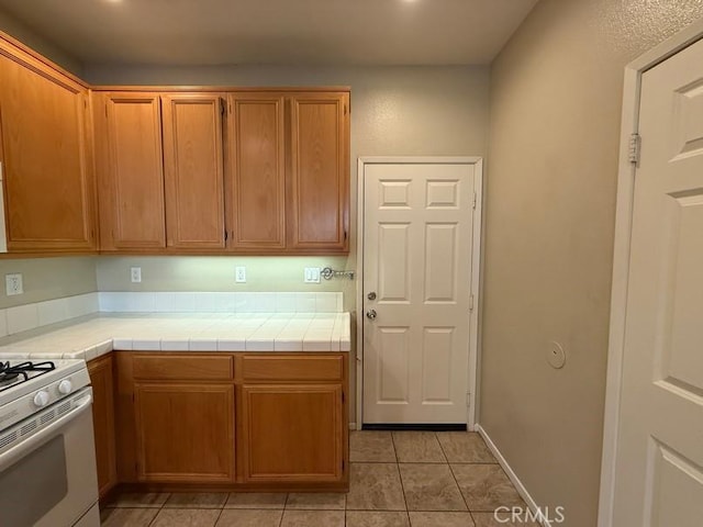 kitchen featuring white gas range, tile counters, and light tile patterned floors