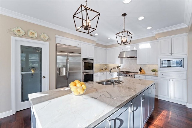 kitchen featuring a center island with sink, sink, built in appliances, and light stone counters