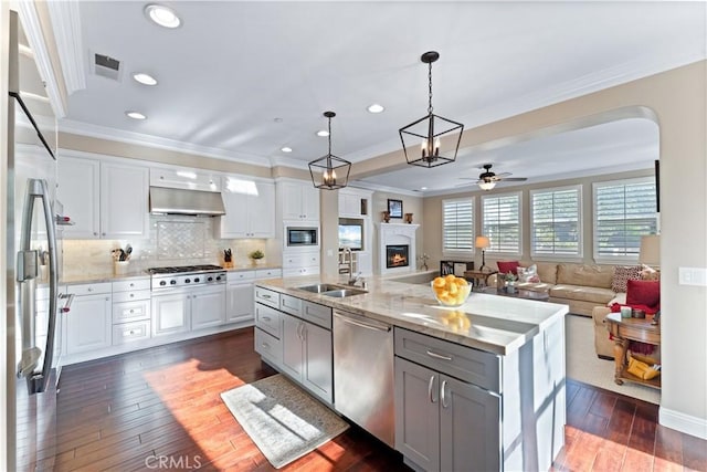 kitchen featuring white cabinetry, decorative light fixtures, a center island with sink, stainless steel appliances, and range hood