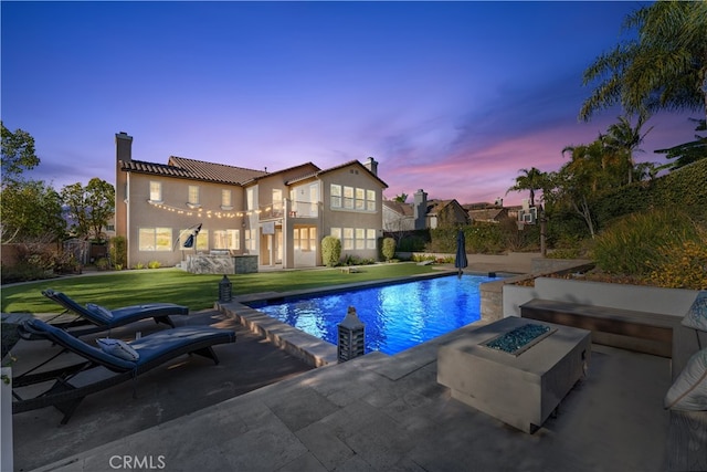 pool at dusk featuring a lawn, a patio area, and an outdoor fire pit