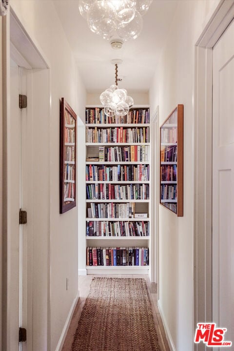 corridor with built in shelves and a chandelier