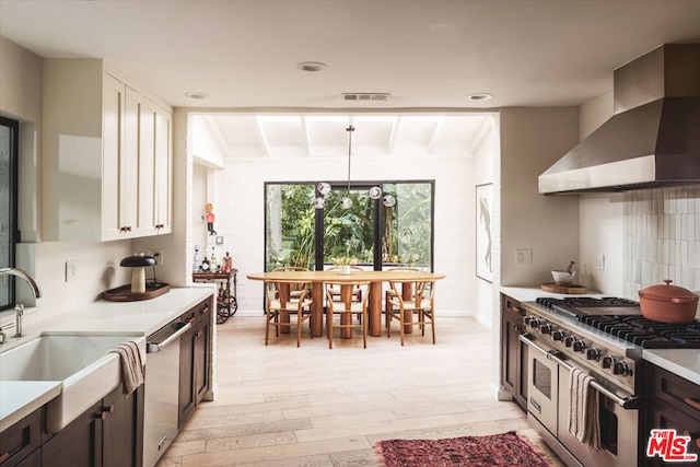 kitchen with dark brown cabinetry, lofted ceiling with beams, appliances with stainless steel finishes, pendant lighting, and wall chimney range hood