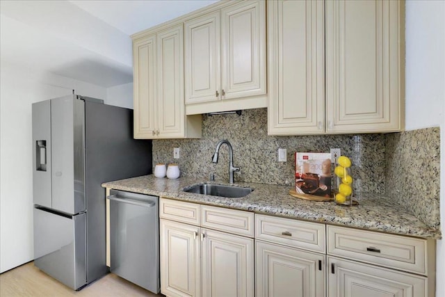 kitchen featuring sink, stainless steel appliances, light stone counters, decorative backsplash, and cream cabinetry