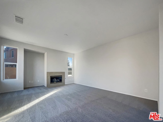 unfurnished living room featuring a tiled fireplace and dark colored carpet