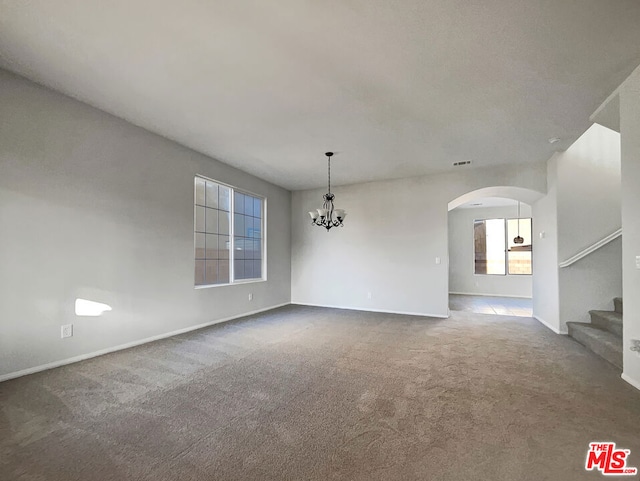 carpeted spare room featuring an inviting chandelier