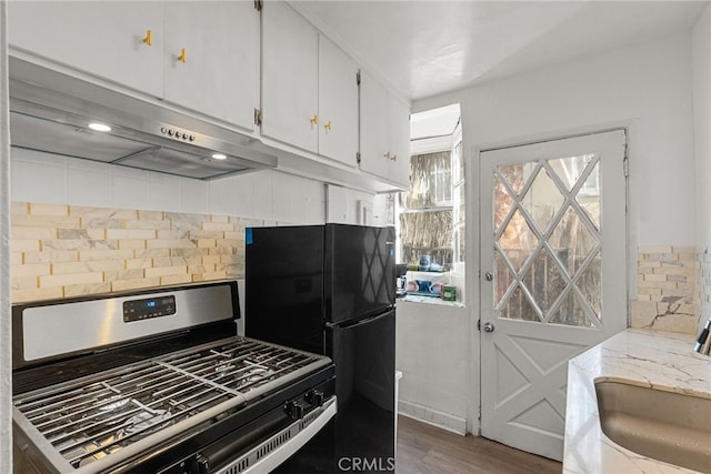 kitchen with black refrigerator, dark hardwood / wood-style floors, stainless steel gas stove, white cabinets, and decorative backsplash