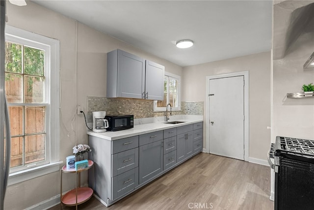 kitchen featuring tasteful backsplash, gray cabinets, stainless steel gas range, and sink