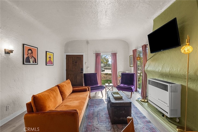 living room featuring wood-type flooring, heating unit, and a textured ceiling