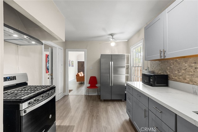 kitchen featuring gray cabinets, stainless steel appliances, light stone counters, light hardwood / wood-style floors, and wall chimney exhaust hood