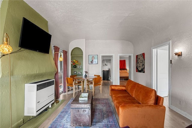 living room with built in shelves, hardwood / wood-style floors, heating unit, and a textured ceiling