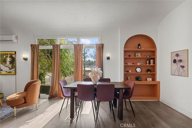 dining space with built in shelves, wood-type flooring, an AC wall unit, and a textured ceiling