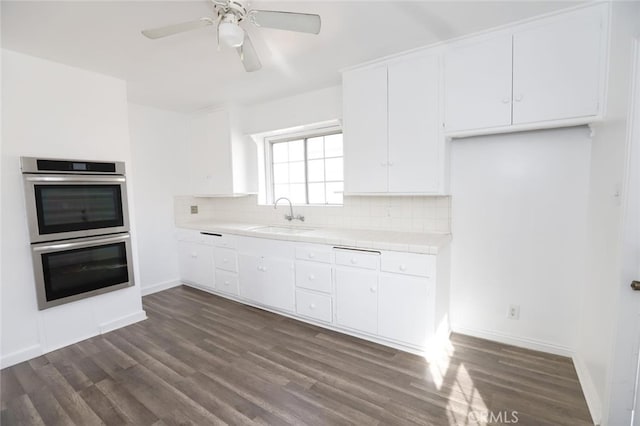 kitchen with dark hardwood / wood-style floors, double oven, sink, white cabinets, and decorative backsplash