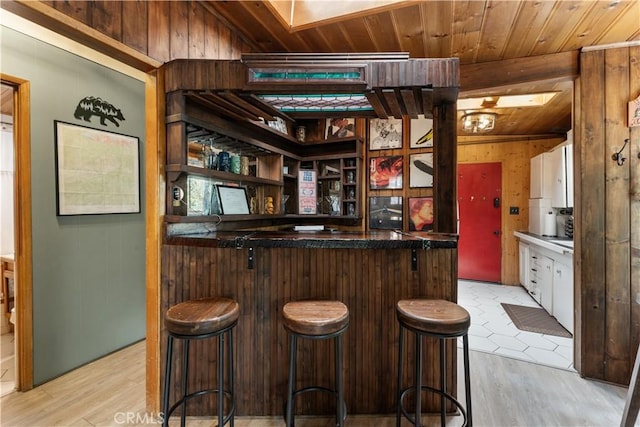 bar with wood ceiling, light hardwood / wood-style flooring, wooden walls, and white cabinets