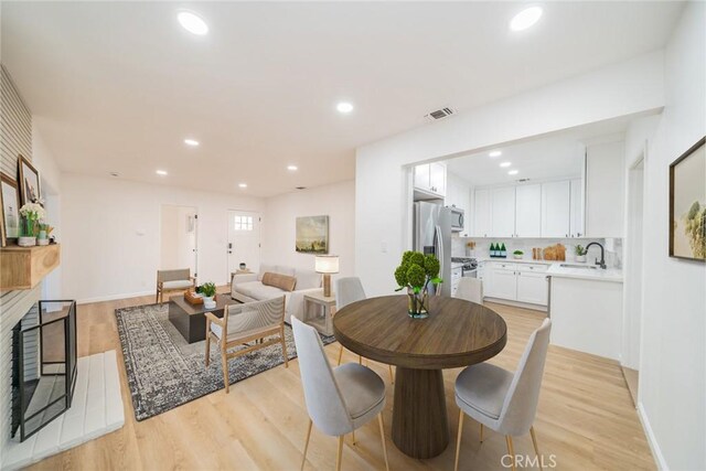 dining space featuring sink, light hardwood / wood-style flooring, and a brick fireplace