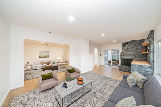 living room with a stone fireplace and light wood-type flooring