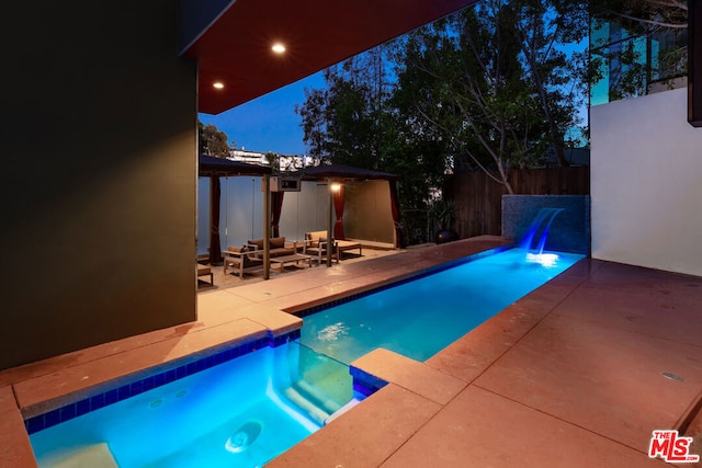 pool at night with an outdoor living space and a patio