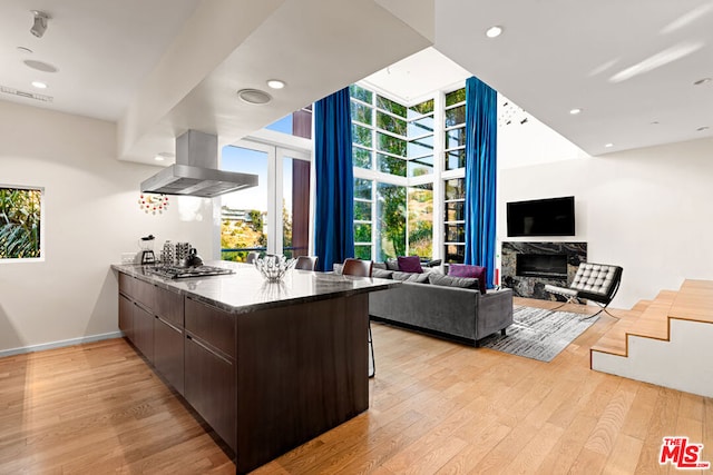 kitchen with dark brown cabinets, island range hood, a high end fireplace, kitchen peninsula, and light wood-type flooring