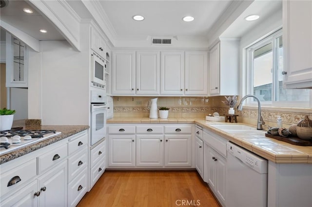 kitchen featuring sink, tile countertops, white appliances, light hardwood / wood-style floors, and white cabinets