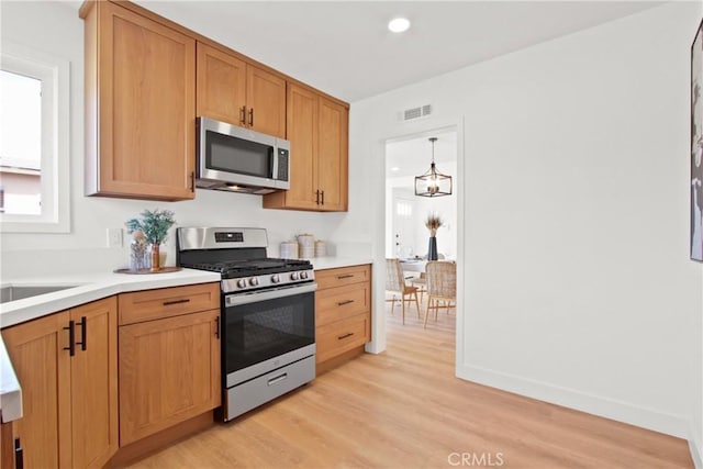 kitchen with stainless steel appliances, decorative light fixtures, light hardwood / wood-style floors, and a notable chandelier