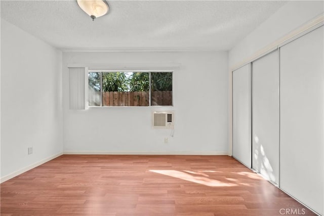 unfurnished bedroom featuring a closet, light hardwood / wood-style floors, a wall unit AC, and a textured ceiling