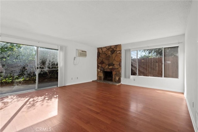 unfurnished living room with hardwood / wood-style floors, a stone fireplace, and a wall mounted AC