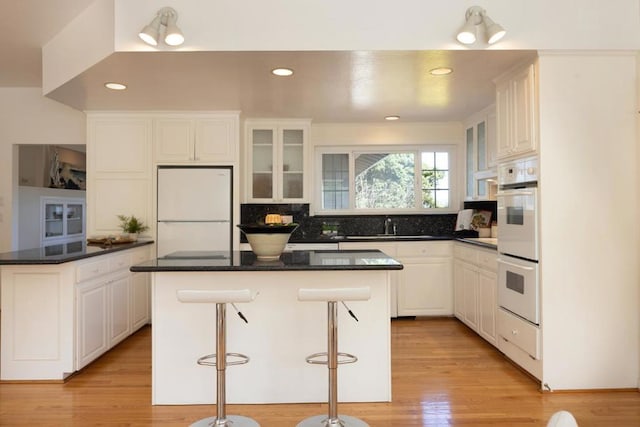 kitchen featuring a breakfast bar area, white cabinetry, a center island, light hardwood / wood-style flooring, and white appliances