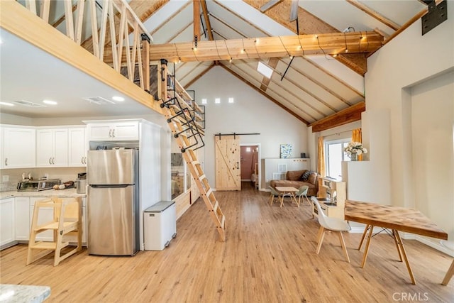 kitchen featuring high vaulted ceiling, light wood-type flooring, stainless steel fridge, a barn door, and white cabinets