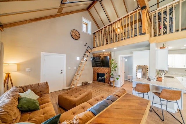 living room featuring beamed ceiling, sink, high vaulted ceiling, and light hardwood / wood-style floors