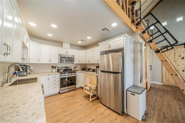 kitchen with sink, light stone countertops, white cabinets, and appliances with stainless steel finishes