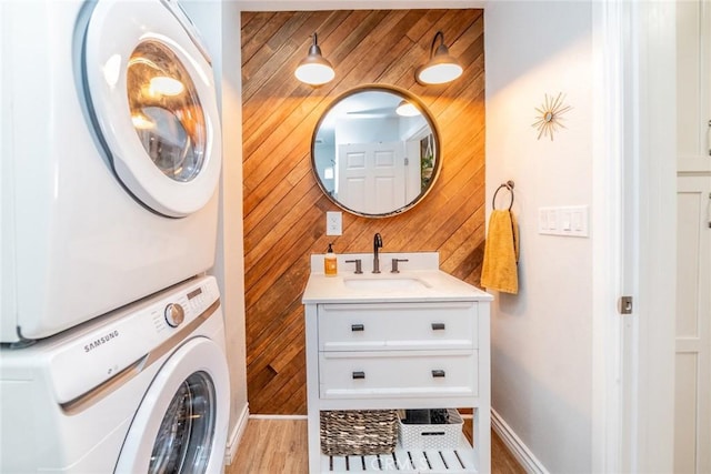 clothes washing area featuring stacked washer and dryer, sink, and wood walls