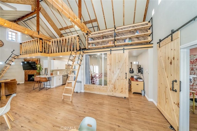 interior space with light hardwood / wood-style floors, beam ceiling, high vaulted ceiling, and a barn door