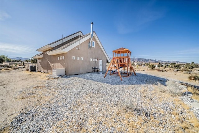 rear view of property featuring a mountain view, central air condition unit, and a playground