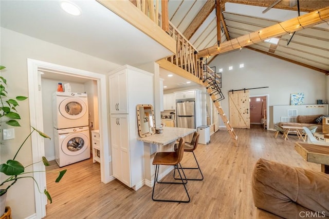 interior space featuring stacked washer and clothes dryer, white cabinetry, high vaulted ceiling, stainless steel fridge, and a barn door