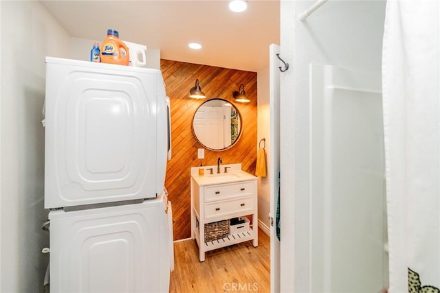 bathroom with vanity, stacked washer / drying machine, hardwood / wood-style flooring, and wood walls