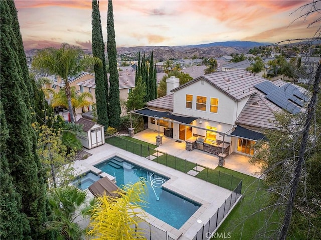 back house at dusk with a swimming pool with hot tub, a yard, a patio, and a shed