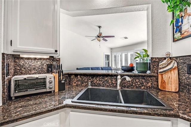 kitchen with sink, ceiling fan, backsplash, white cabinets, and dark stone counters