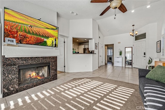 living room featuring ceiling fan with notable chandelier, high vaulted ceiling, a fireplace, light tile patterned floors, and a textured ceiling