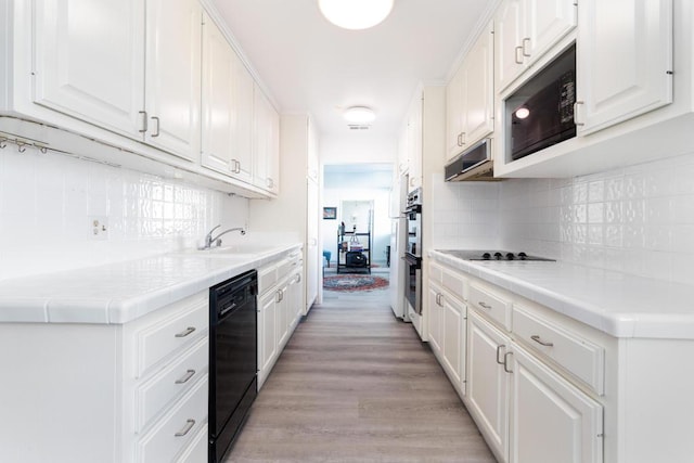 kitchen featuring tile countertops, sink, white cabinets, black appliances, and light hardwood / wood-style flooring