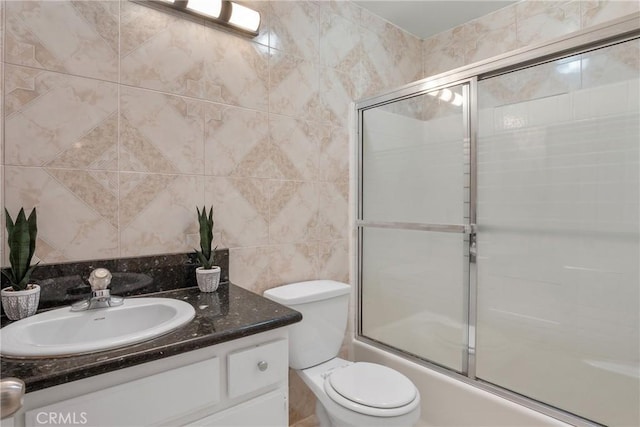 full bathroom with tile walls, vanity, shower / bath combination with glass door, and toilet