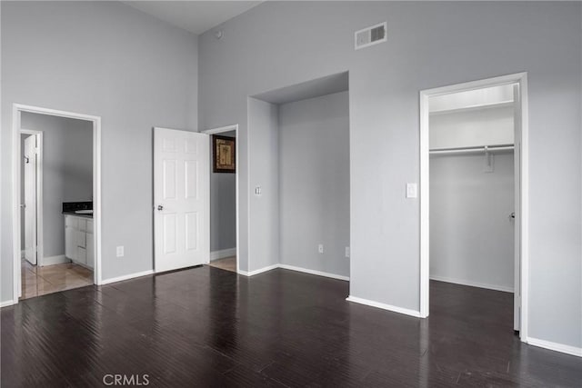 unfurnished bedroom featuring a towering ceiling, connected bathroom, dark hardwood / wood-style flooring, and a closet