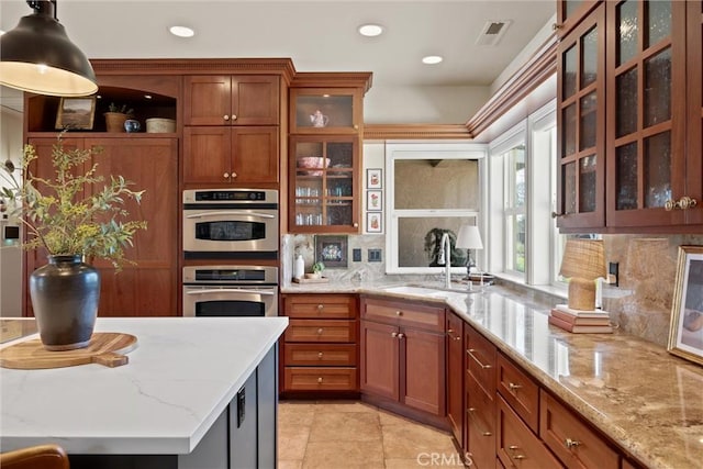 kitchen featuring sink, decorative backsplash, hanging light fixtures, light stone countertops, and stainless steel double oven