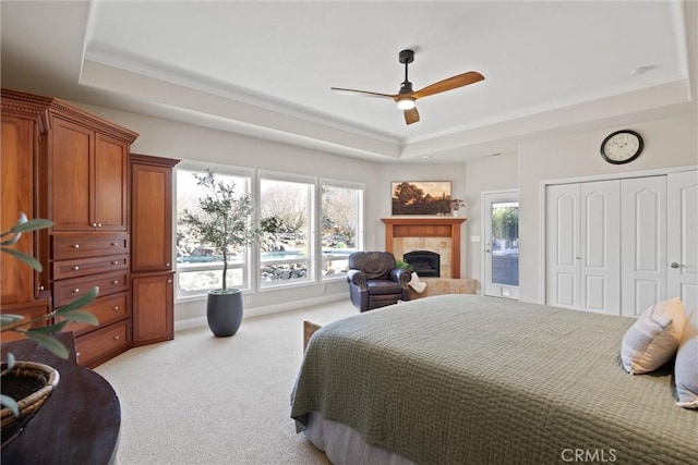 bedroom featuring multiple windows, ceiling fan, a tray ceiling, and light carpet