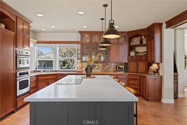 kitchen with sink, black electric cooktop, double oven, a kitchen island, and pendant lighting