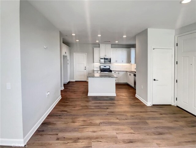 kitchen featuring dark stone countertops, backsplash, stainless steel appliances, a center island, and white cabinets